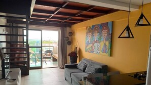 A modern living room with a sofa, a kitchen area, and a balcony with a view. - Laguna Beach - Charming, furnished, and cozy loft-style apartment - 402 (Ipojuca)