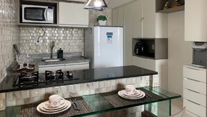 A modern kitchen with a black countertop, a glass dining table, a microwave, a refrigerator, and pendant lighting. - Laguna Beach - Charming, furnished, and cozy loft-style apartment - 402 (Ipojuca)