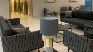 Una sala de estar moderna con un sofá, sillones, una mesa de centro y una lámpara. Hay un cuadro en la pared y una escalera que lleva a un ascensor.