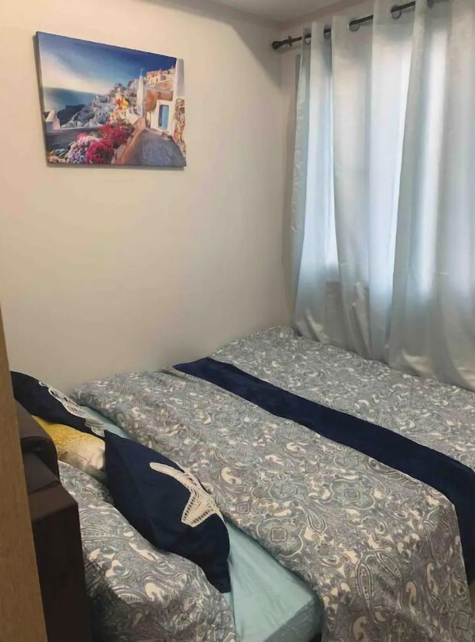 A room with a bed, a painting on the wall, and a window with curtains.