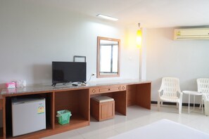 A room with a desk, a television, a small refrigerator, a trash bin, and two white chairs.
