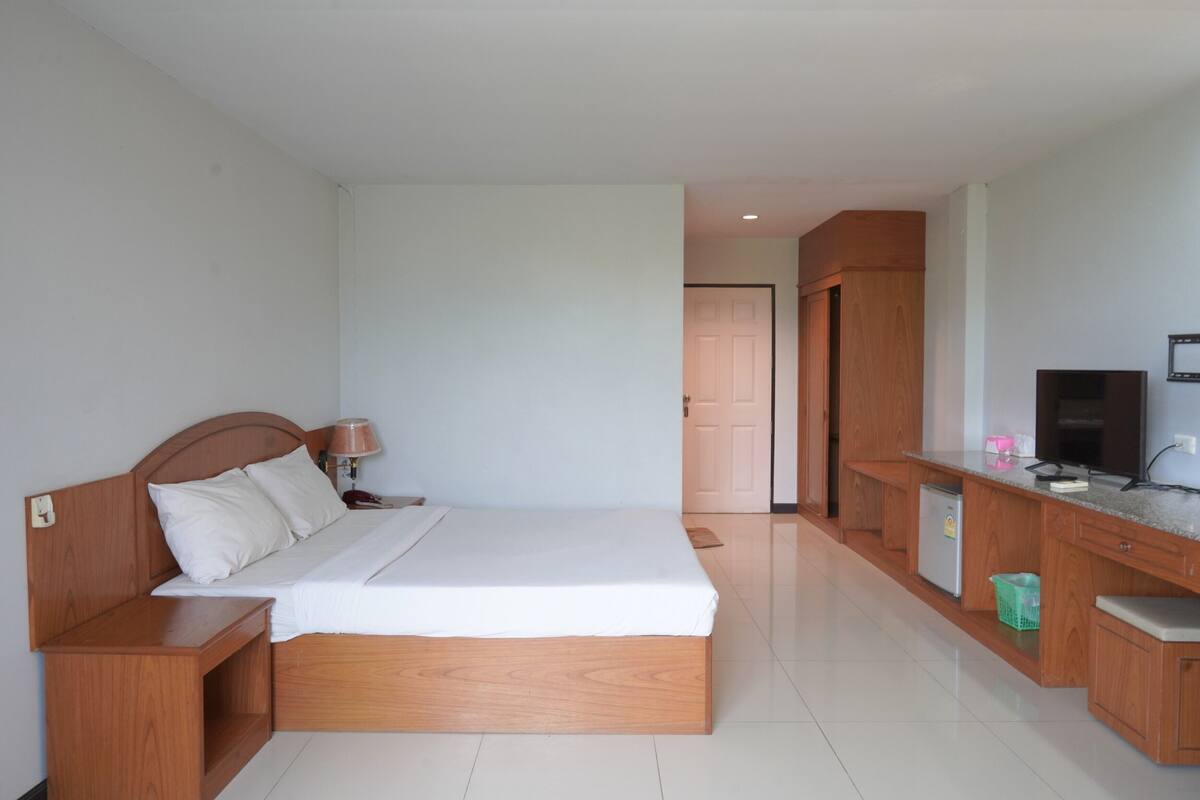 A bedroom with a wooden bed, bedside table, lamp, and a TV on a wooden cabinet.