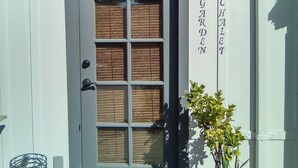 Un edificio con una puerta gris oscuro, una ventana con persianas de madera y un cartel que dice "GARDEN CHALLENGES".