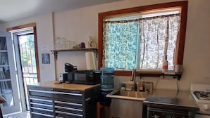 Una cocina compacta con un lavabo, estufa y encimera. Hay una ventana con cortinas, una puerta que da al exterior y un pequeño armario.