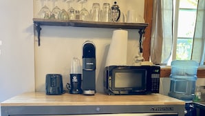 Una zona de cocina con microondas, cafetera y varios utensilios de cocina en un carrito.