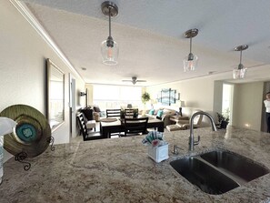 A spacious kitchen with a large island, a dining area, and a living room. There are pendant lights, a ceiling fan, and a view to the outside. - Wake up, fall out of bed... (Siesta Key)