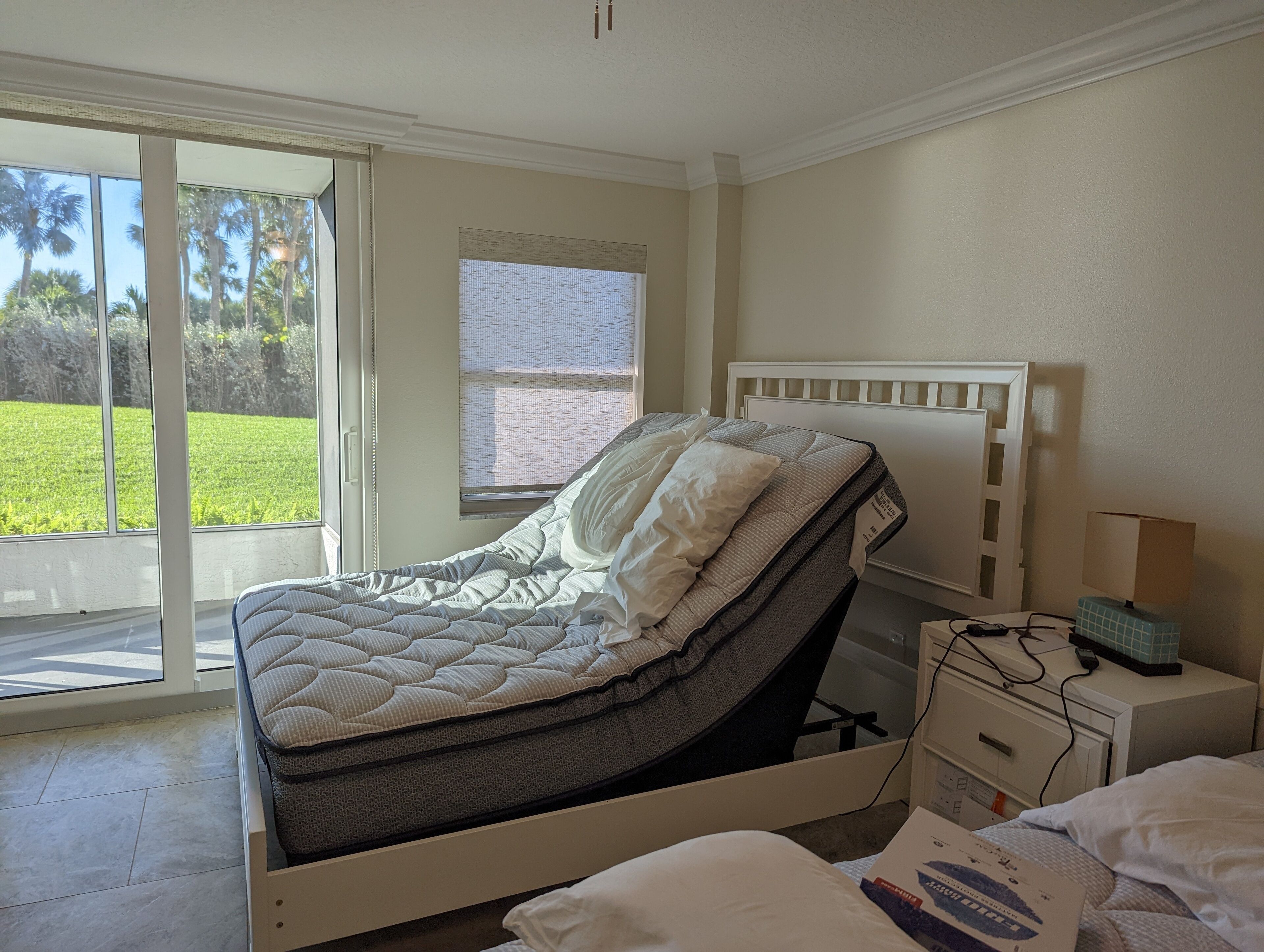 A bedroom with a bed, a nightstand, a lamp, and a window with a view of greenery.
