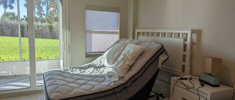 A bedroom with a bed, a nightstand, a lamp, and a window with a view of greenery.