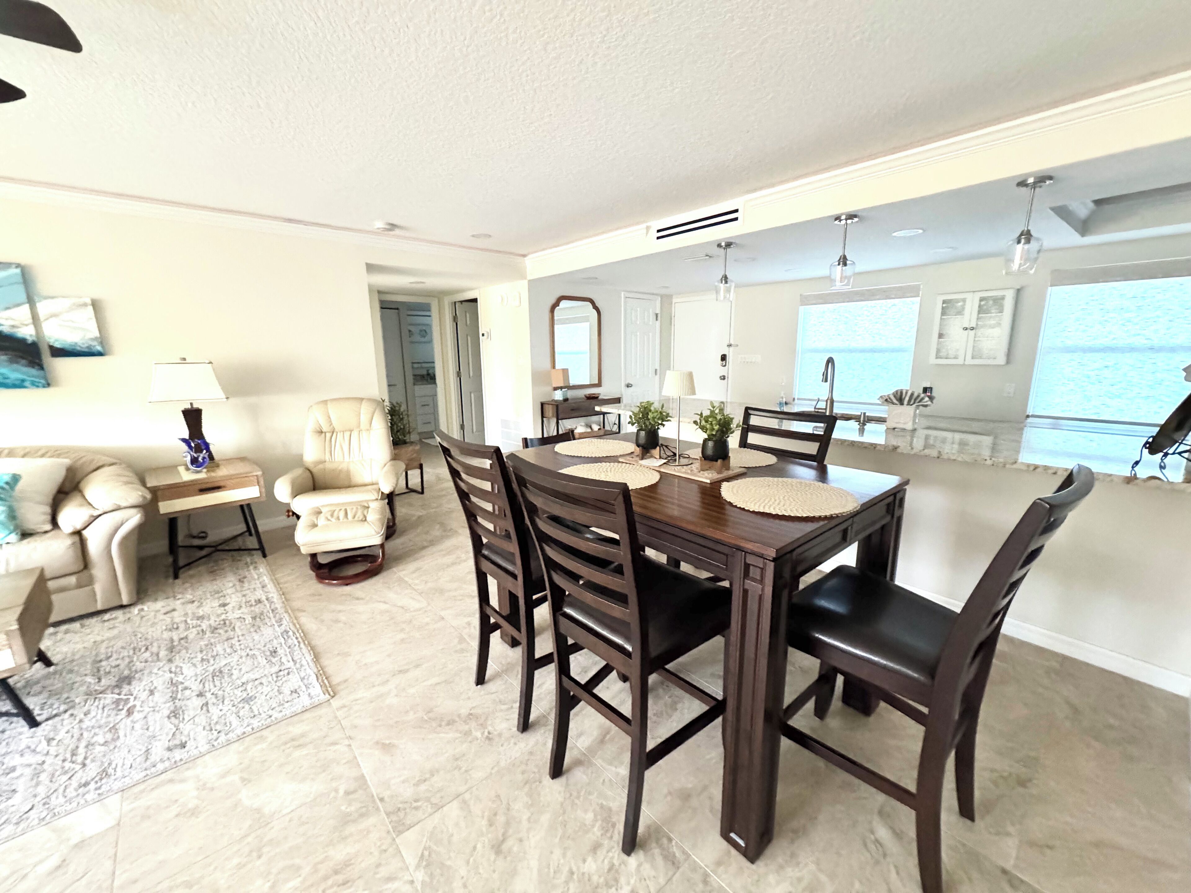 A spacious dining area with a large wooden table, dark chairs, and a view of the ocean through the window.