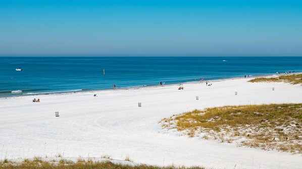 Une plage de sable blanc, avec une eau d’un bleu limpide, et quelques personnes.