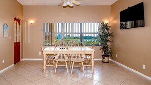A dining area with a table and chairs, a window with a view, a ceiling fan, and a potted plant.