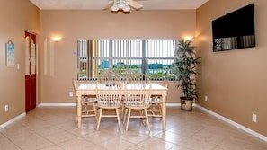 Un coin repas avec une table et des chaises, une fenêtre donnant sur un paysage agréable, un ventilateur de plafond et une plante en pot.