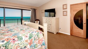 A bedroom with a bed, a dresser, a TV, and a door.