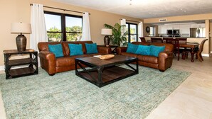 A living room with a brown leather sofa, a coffee table, and a dining area with a wooden table and chairs.