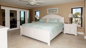A bedroom with a bed, a nightstand, a ceiling fan, a window with blinds, and a door leading to a balcony.