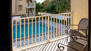 A balcony with a view of a swimming pool, a chair, and a building with multiple balconies. - The Villas A-5 - Premium Plus 3 Bed/2 Bath Oceanfront Condo (Clearwater)