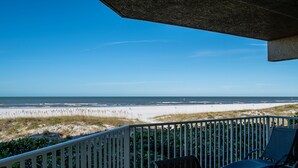 A beach view from a balcony with a railing, a chair, and a view of the ocean.