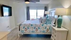 A bedroom with a bed, a nightstand, a lamp, a ceiling fan, a TV, and a window with curtains.