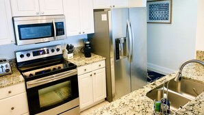 A modern kitchen with white cabinets, stainless steel appliances including a microwave, oven, and refrigerator, a granite countertop, and a stainless steel sink.