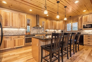 A kitchen with wooden cabinets, a granite countertop, and a central island with bar stools. - Claralea Lodge by Taylor Made Deep Creek (Oakland)