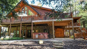 A cabin with a wooden deck, a hot tub, and a stone foundation. - Claralea Lodge by Taylor Made Deep Creek (Oakland)