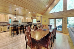 A spacious kitchen with wooden cabinets, a dining area with a large table and chairs, and a view through a glass door. - Claralea Lodge by Taylor Made Deep Creek (Oakland)