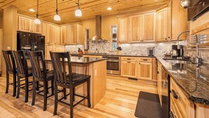 A modern kitchen with wooden cabinets, a central island, and pendant lighting. - Claralea Lodge by Taylor Made Deep Creek (Oakland)