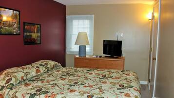 A bedroom with a floral bedspread, a wooden dresser, a television, and two framed pictures on the wall.