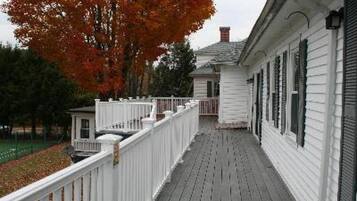 Um deck de madeira com guarda-corpo branco, um pequeno edifício com chaminé e uma árvore com folhas de outono.