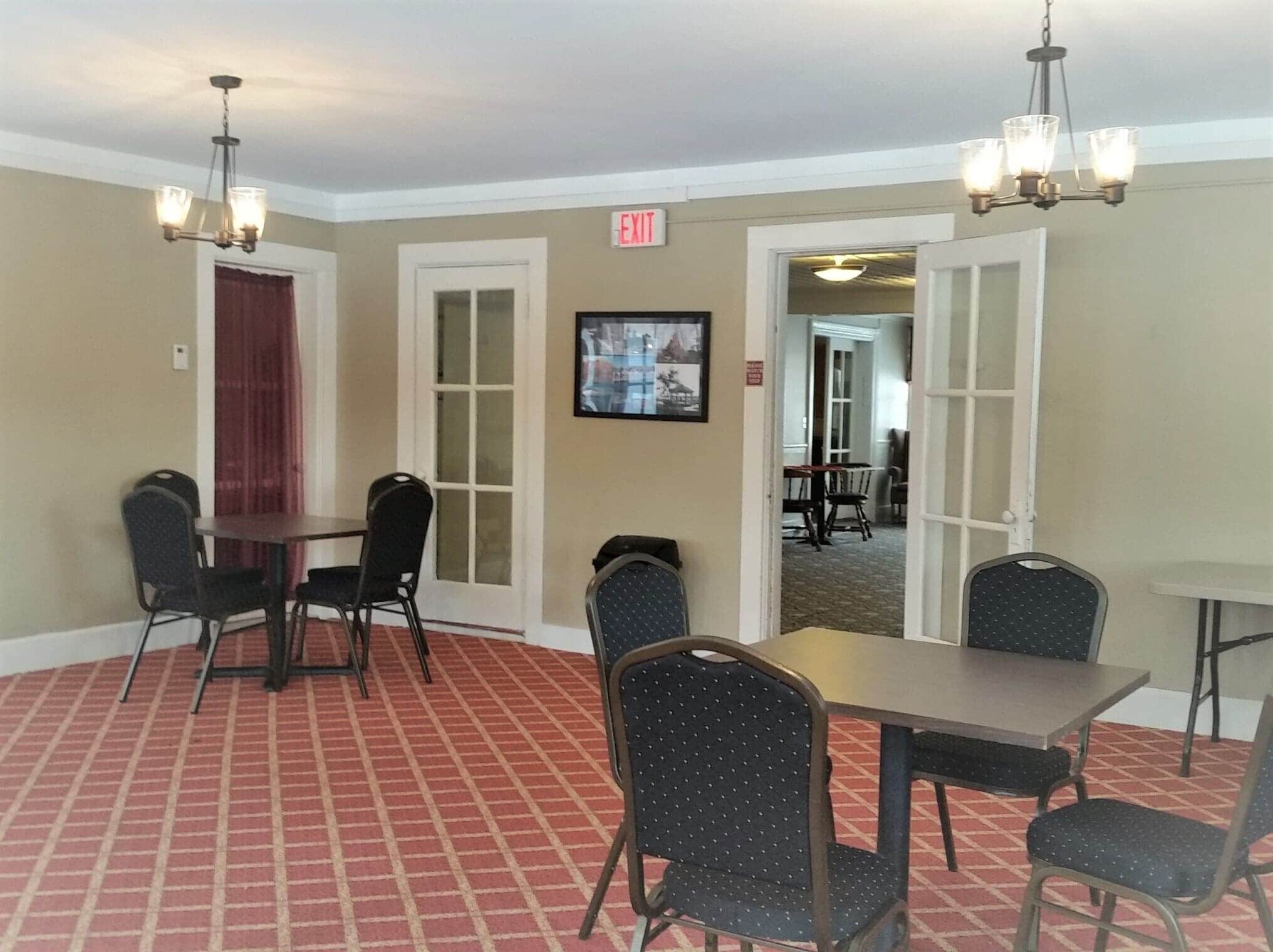 A hotel room with a red patterned carpet, a dining area with a table and chairs, and an exit sign on the wall.