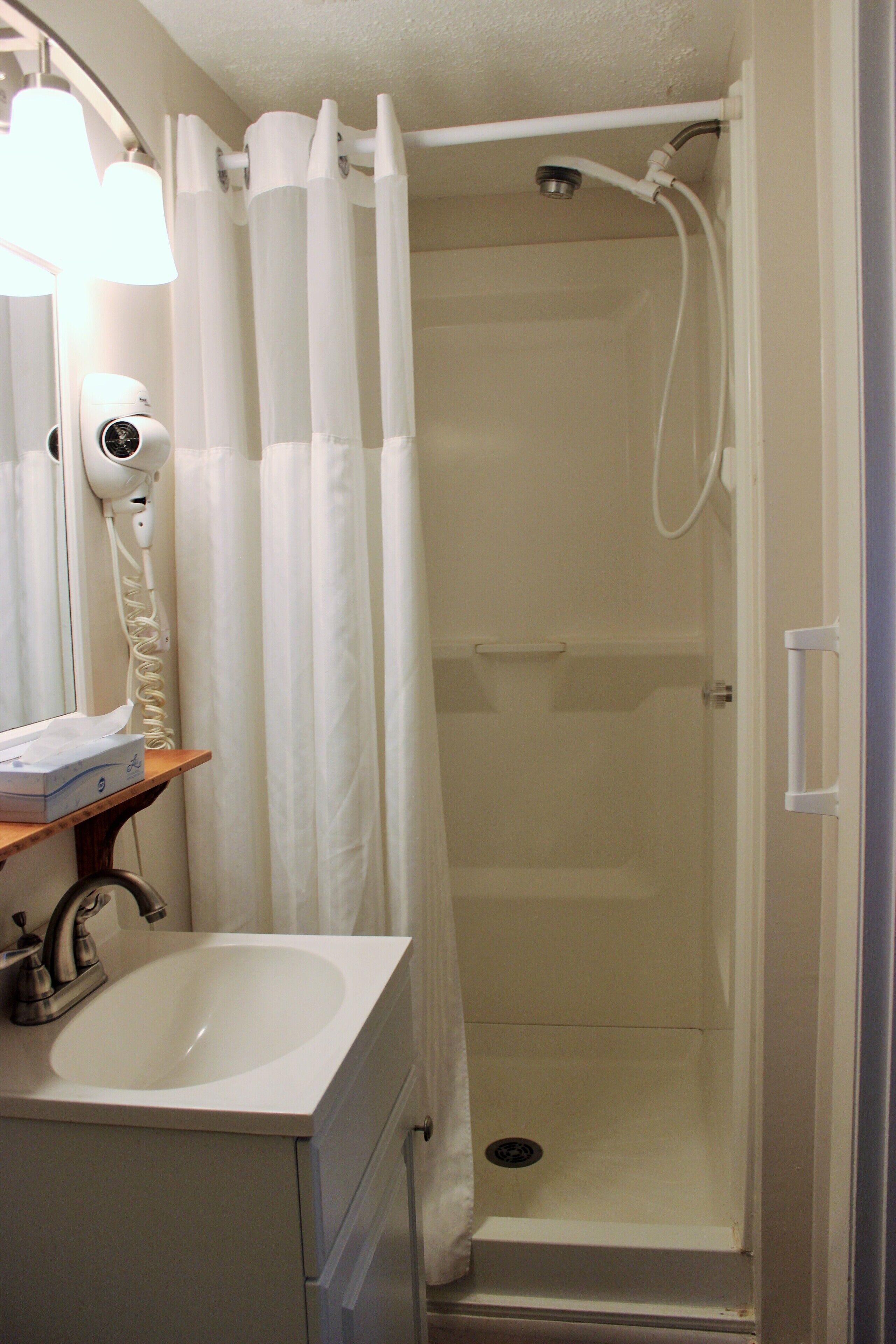 A bathroom with a shower, a sink, a hairdryer, and a mirror.