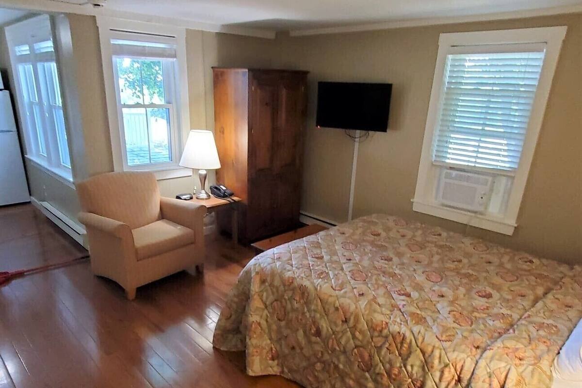 Ein Schlafzimmer mit Bett, Stuhl, Schreibtisch, Fernseher und Fenster.