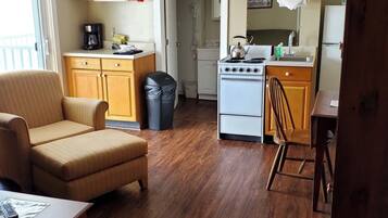 Un espacio habitable compacto con kitchenette, un sofá, una mesa de comedor y un cubo de basura.