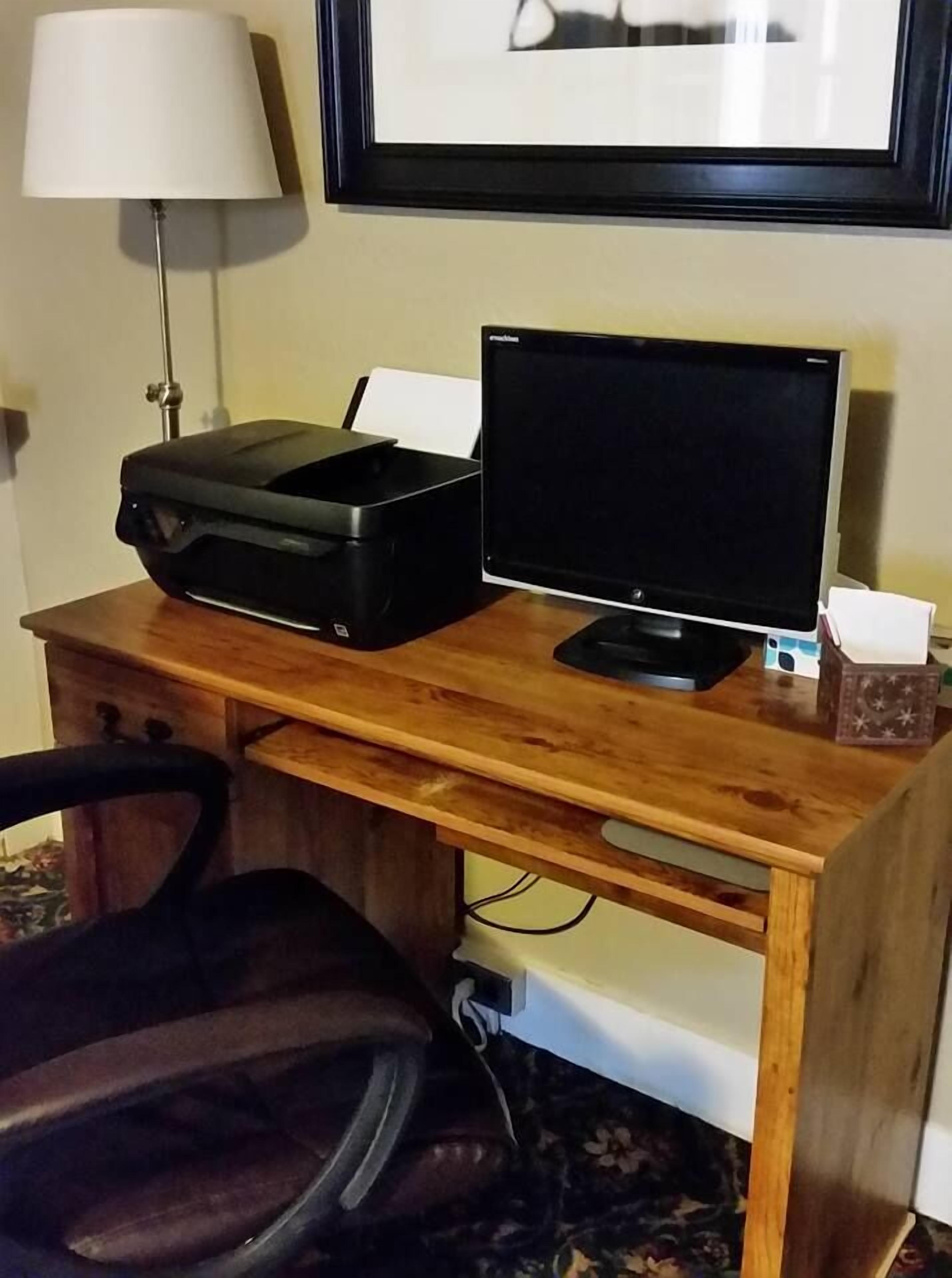 Un bureau en bois avec une imprimante, un écran et une lampe.