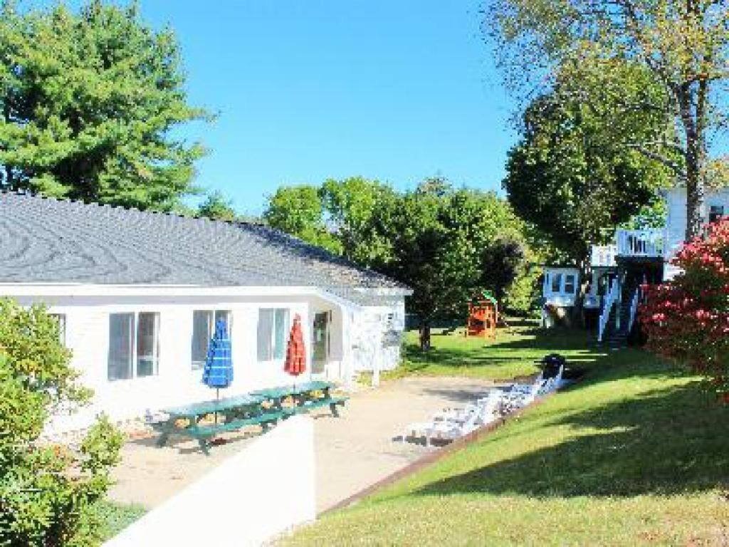 A white building with a covered outdoor seating area, a small pool, and a well-maintained lawn.