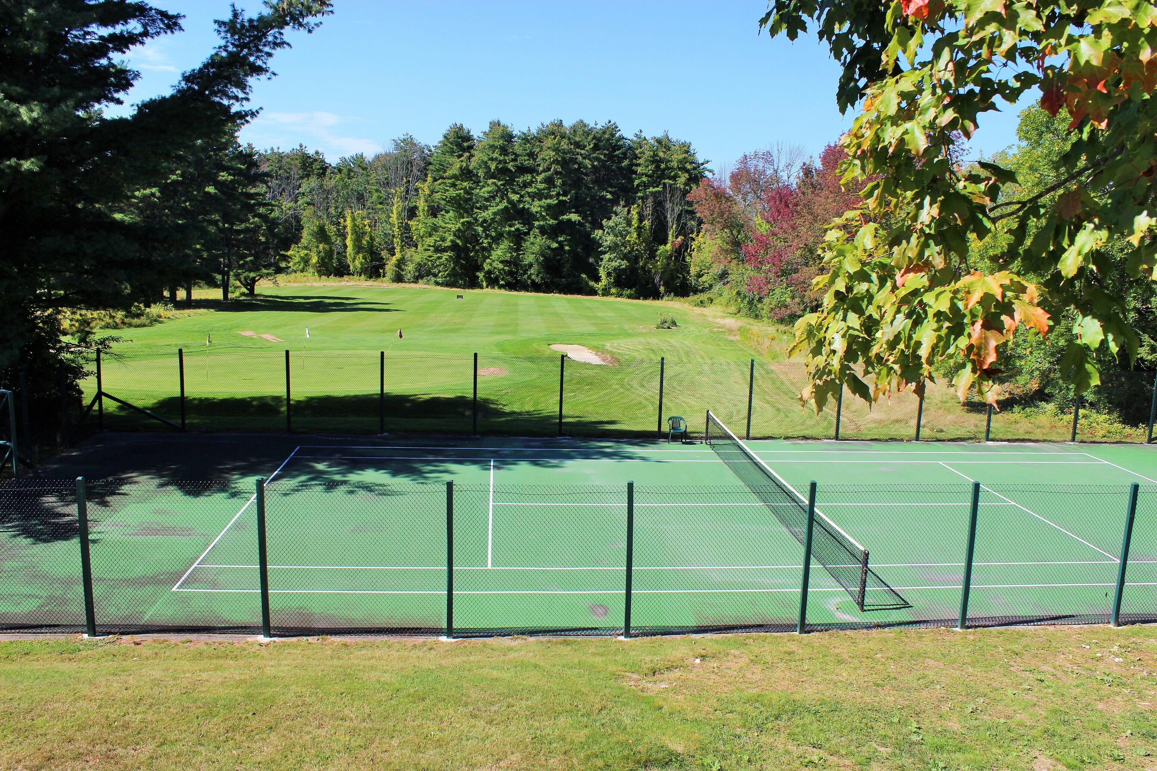 A tennis court with a net, surrounded by a fence, and trees in the background.