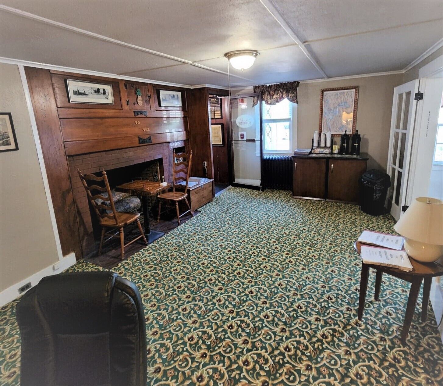 Una habitación con alfombra estampada, chimenea, muebles de madera y una ventana con cortinas.