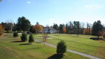 A golf course with a house in the background, surrounded by trees and a clear sky.