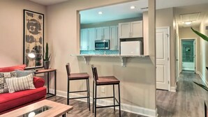 A modern kitchen with white cabinets, a microwave, and a countertop. There is a red sofa with a coffee table and two bar stools. - NEW! Modern Charlotte Hub in Lockwood Neighborhood (Charlotte)