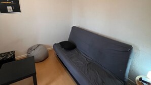 Una habitación pequeña y poco amoblada con un sofá gris, una mesita y un sillón informal.