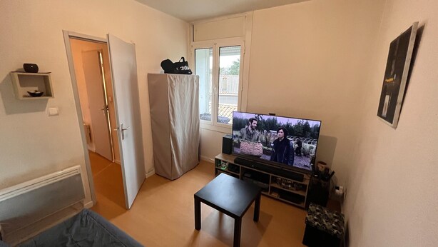 Un salón pequeño con televisor, una mesita, sofá y refrigerador.