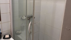 Un box de ducha con paredes de vidrio, un lavabo blanco con un jabonera, y una botella verde de champú en el suelo.