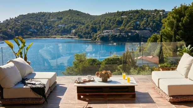 A terrace with a view of a lake, furnished with two sofas and a coffee table, and a glass railing. - Ideal location close to the beach (Skiathos)