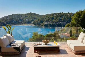 A terrace with a view of a lake, furnished with two sofas and a coffee table, and a glass railing. - Ideal location close to the beach (Skiathos)