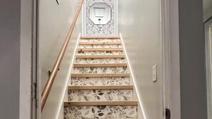 Una escalera con alfombra de motivos florales y escalones de madera que conducen a un rellano con un espejo decorativo de ocho lados.