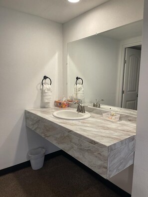 A bathroom with a marble sink, two towel racks, a mirror, and a trash bin.