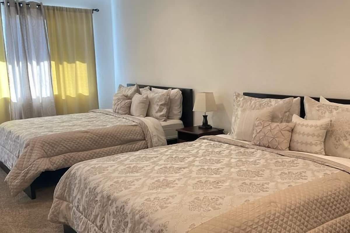 A hotel room with two beds, each with a quilted bedspread and matching pillows. There is a nightstand with a lamp between the beds.