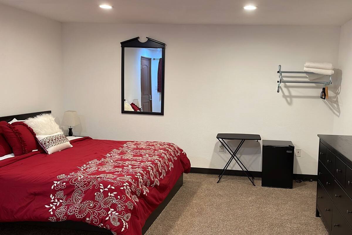 A bedroom with a bed, a mirror, a dresser, a small table, and a wall-mounted towel rack.
