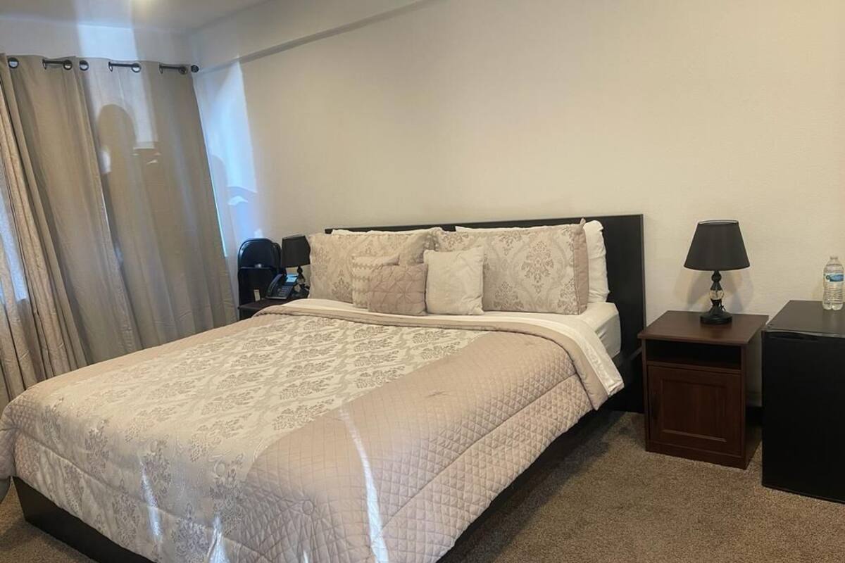 A neatly made bed with a quilted cover, a bedside table with a lamp, and a water bottle on a nightstand.