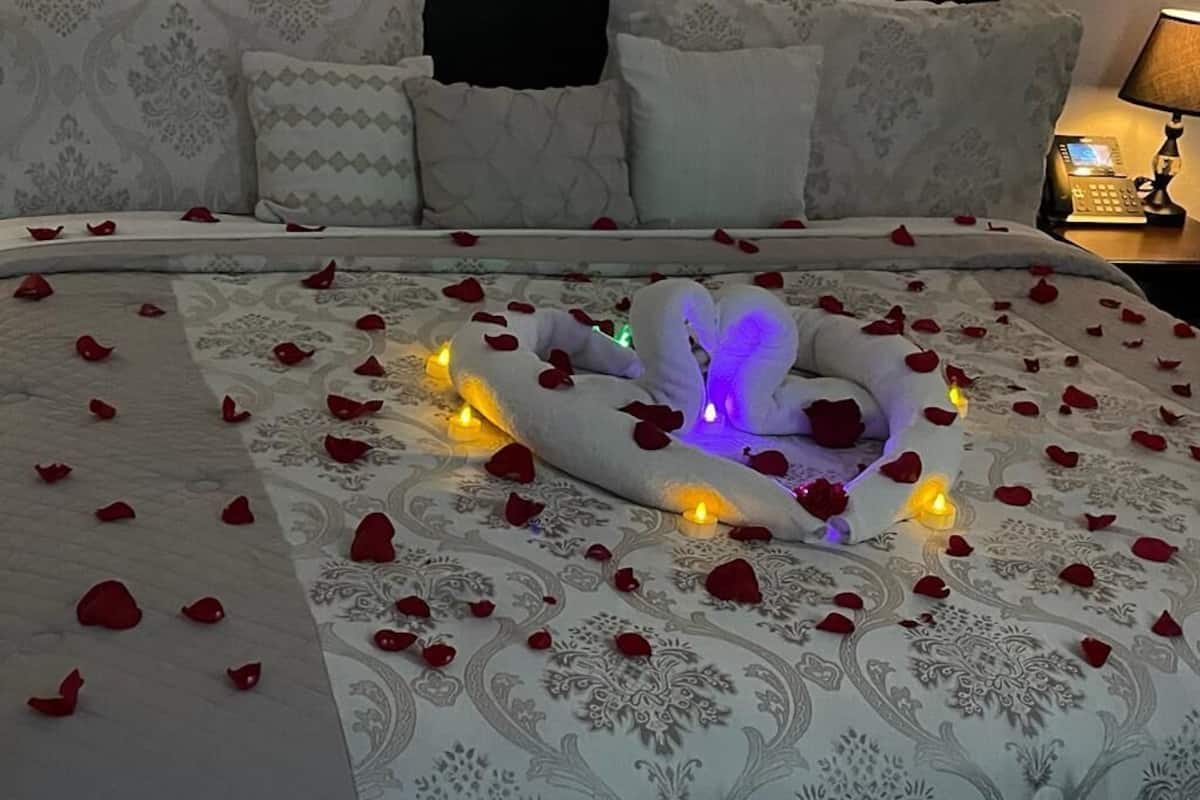 A bed with rose petals and candles, a telephone, and a lamp on a bedside table.